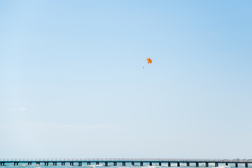 Fototapeta na wymiar Paraglider flying through the sky over the sea and the pier on a Sunny summer day.