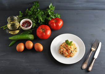Ingredients for cooking traditional Turkish fried eggs with tomatoes. In the frame, eggs, tomatoes, hot green peppers, greens, olive oil, spices and a plate of cooked scrambled eggs. View from above.