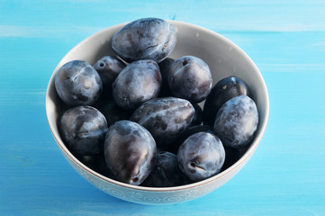 Ripe plums in a white deep bowl. Blue wood background. Close-up. Macro photography.