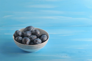 Ripe plums in a deep bowl. Blue wood background. Free space for text. Close-up.