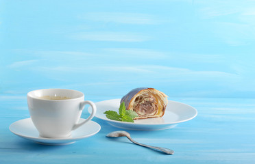 On the plate is half an airy and layered chocolate croissant. Next cup with coffee and a teaspoon. Blue wood background. Close-up.