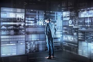Obraz premium Making decision. Calm concentrated young programmer with virtual reality glasses standing in front of a giant transparent screen and thoughtfully looking at it while making important decision