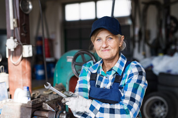 Senior female mechanic repairing a car in a garage.