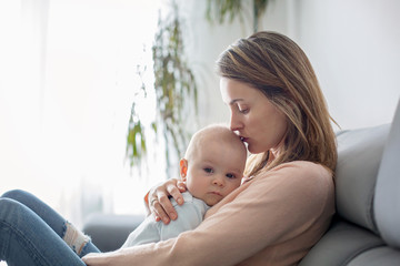 Young mother, holding her sick toddler boy, hugging him at home
