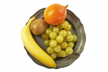 Kiść zielonych winogron, granadilla, kiwi i banan na metalowym talerzu, centralnie z góry na białym tle