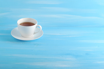 Cup and saucer made of white porcelain. In the cup black tea. Blue wood background. There is free space for text.