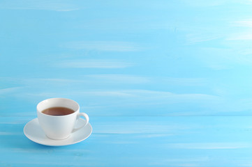 Cup and saucer made of white porcelain. In the cup black tea. Blue wood background. There is free space for text.