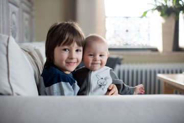 Little baby boy and his older brother, sitting on a couch in sunny living room