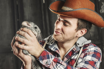 Portrait of a Cowboy. dark hair, jeans , plaid shirt. he holds the chinchilla animal