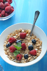 Oat flakes with raspberries and blueberries. The dish is decorated with a mint leaf. In the background is a cup with berries. Blue wood background. View from above. Close-up.
