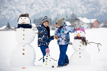 Family with children, building snowman in the park in little village in Austria