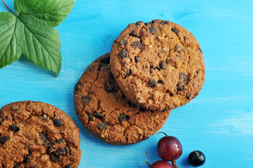 Oat cookies with chocolate chips. A few berries of gooseberries and black currant. Blue wood background. View from above. Close-up. Macro photography.