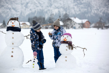 Family with children, building snowman in the park in little village in Austria