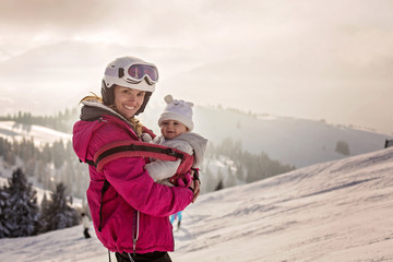 Fototapeta na wymiar Young mother, carrying her baby boy in sling, climbing on peak wintertime, Austrian Apls