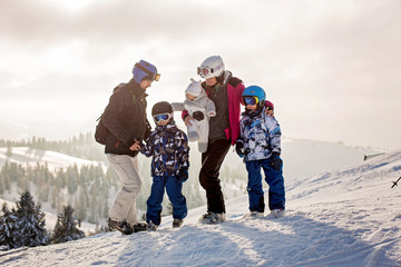 Beautiful family with kids, skiing in a scenery area in Austrian Alps on sunset, enjoying the view - obrazy, fototapety, plakaty
