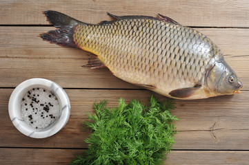 Carp on a wooden surface. Next to the greens of dill and mortar with salt and pepper. Carp is the perfect Christmas dish. View from above. Close-up.