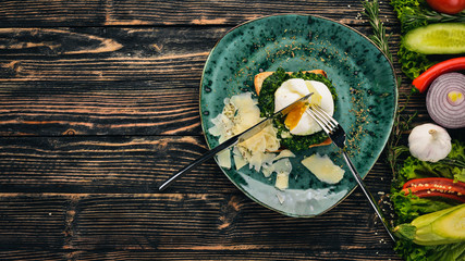 Breakfast. Toast Bread with Spinach, Poached Egg and Parmesan Cheese. On a black wooden background. Copy space.