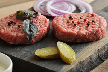 On a wooden board, two hamburger cutlets, cucumber slices marinated, onion rings red. On one of the cutlets is a basil leaf. Close-up. Macro photography.