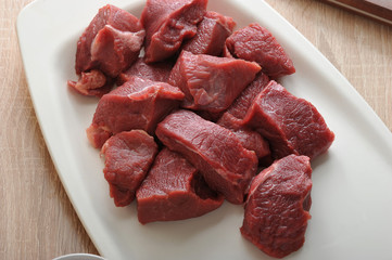 On a white plate slices of raw beef. Meat for making minced meat or goulash. There is a knife for cutting meat. View from above. Close-up. Macro photography.