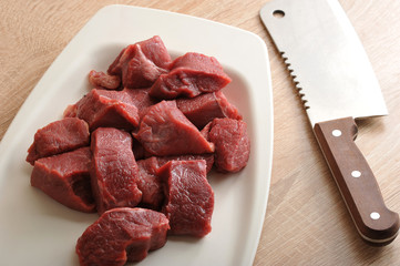 On a white plate slices of raw beef. Meat for making minced meat or goulash. There is a knife for cutting meat. View from above. Close-up. Macro photography.