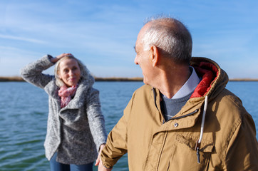 Portrait of happy senior couple by the lake on sunny autumn day.