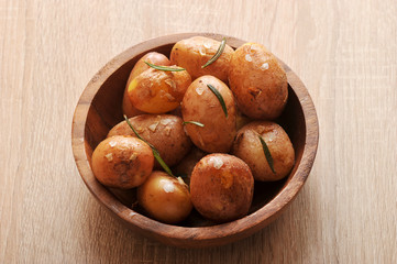 Potatoes in a wooden bowl. Prepared in a peel with sea salt, garlic and rosemary.  Light wooden background. Closeup.