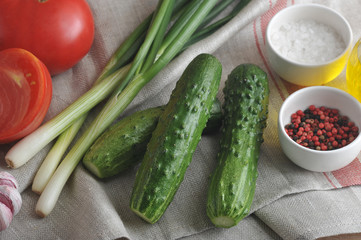 Fresh cucumbers, green onions and red tomatoes on a cloth napkin. Near the saucer with salt and pepper. View from above. Close-up.