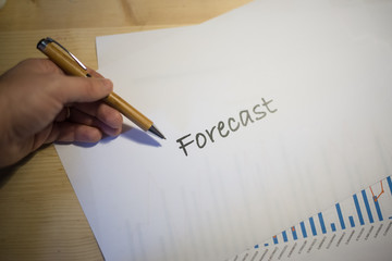 Male hands holding a white sheet of paper with Forecast text on it duing a business meeting