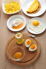 Variants of cooking dishes from chicken eggs. Omelette, soft-boiled, hard-boiled, fried, scrambled eggs. In a glass bowl, a raw egg without a shell. Close-up. Vertical shot.