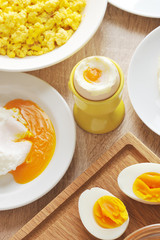 Two halves of an hard-boiled eggs, soft-boiled eggs. In the plates, the egg is poached and scrambled eggs. View from above. Light wooden background.