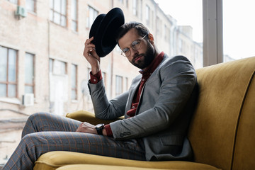 Fototapeta premium fashionable elegant man in eyeglasses and hat sitting on couch