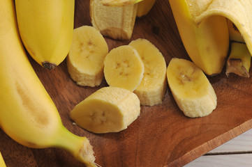 Bananas on a wooden platter. One of the bananas is cleaned and cut into slices. View from above. Close-up. Macro shooting.
