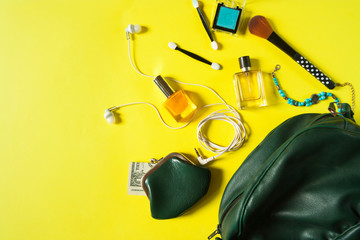 Women's bag and women's accessories - cosmetics, perfumes, headphones, brushes and purse with money on a bright yellow background with space for text. Flat lay