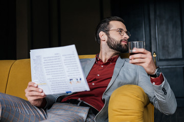 stylish man holding newspaper and glass of cognac