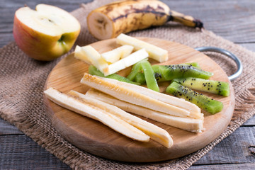 Slices of fruit on a cutting board (kiwi, banana, apple) on a table