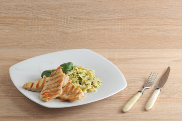 Pasta farfalle with pesto sauce. Next to the chicken meat, cooked on the grill. The dish is decorated with a leaf of fresh basil. View from above. Close-up.
