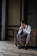 caucasian pensive stylish man sitting in armchair in loft interior