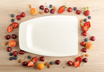 Naklejka na ściany i meble Top view of a white plastic tray. On the edges of the tray are berries: strawberries, blueberries, cherries, apricots and almonds. Beige wood background.