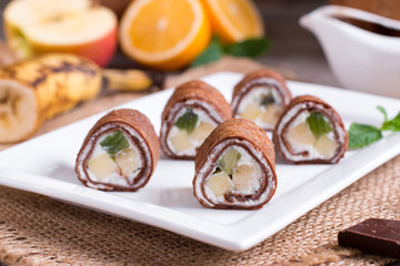 Thin chocolate pancakes rolled on a plate on a wooden background