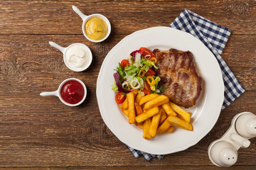 Grilled pork neck served with French fries and salad.