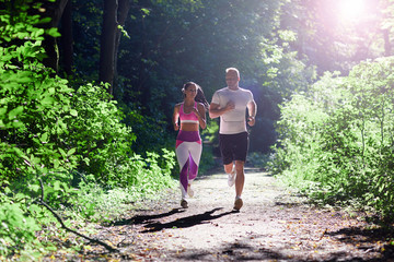 Athletic man and woman doing Jogging in the forest with sun rays.