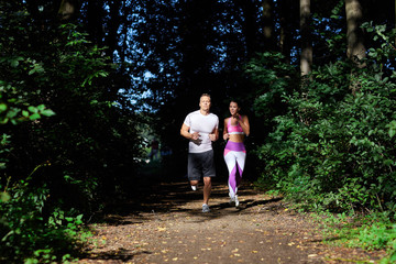A man and a woman sporting on a Sunny day, jog along the forest path.