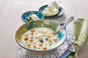 Creamy cauliflower soup in a blue cup with croutons and parmesan