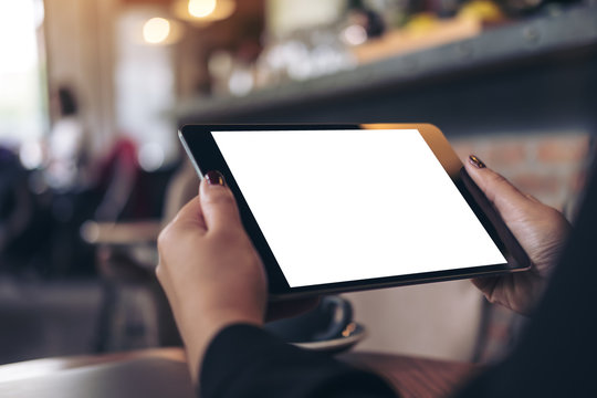 Mockup image of a woman holding black tablet pc with blank white desktop screen in cafe