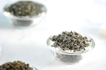 Black tea and green tea in separate glass saucers. Light background. Close-up. Macro photography.