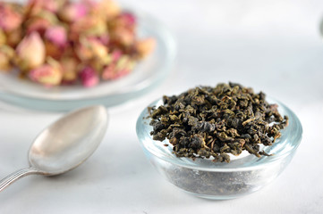 Tea green milky oolong. Near the dried roses buds. In the frame, a teaspoon. Light background. Close-up. Macro photography.