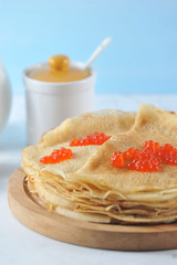 Pancakes thin on a round wooden tray. On the pancakes laid red caviar. Light background. Vertical orientation of the frame. Macro photography.