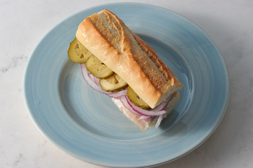 A traditional sandwich with a young herring. On baguette fillets of herring, slices of pickled cucumber, onion rings. Sandwich on a blue plate. Light background. Close-up.