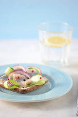 A sandwich with herring on a blue plate. On black bread cream cheese, young herring, fresh...