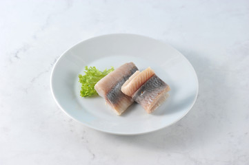 Fillet of Atlantic herring on a white plate. The fish is decorated with a leaf of lettuce. Light...